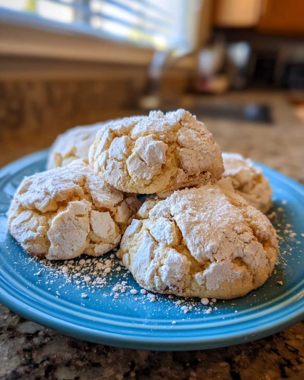 A stack of soft, cracked-top cool whip cookies heavily dusted with powdered sugar, served on a bright blue plate.
