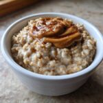 Close-up of creamy banana oatmeal in a white bowl topped with peanut butter and cinnamon.