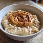 Close-up of creamy banana oatmeal topped with a swirl of peanut butter and a sprinkle of cinnamon.