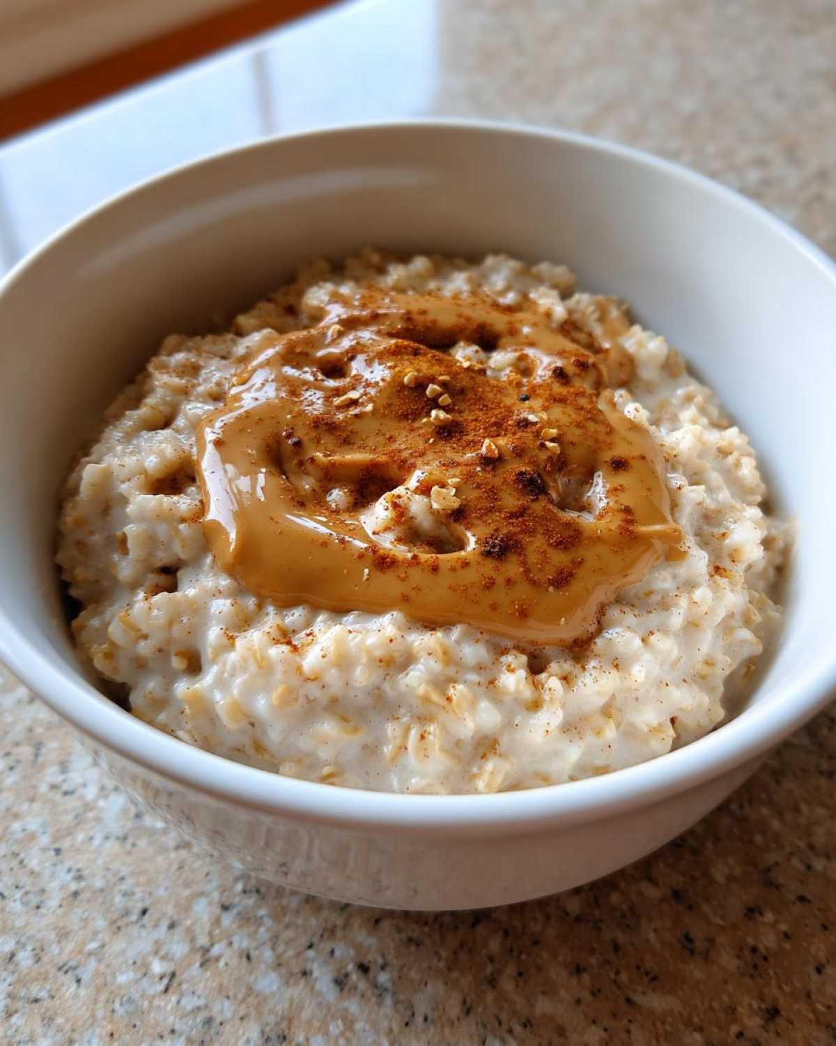 Close-up of a bowl of creamy banana oatmeal topped with melted peanut butter and cinnamon.