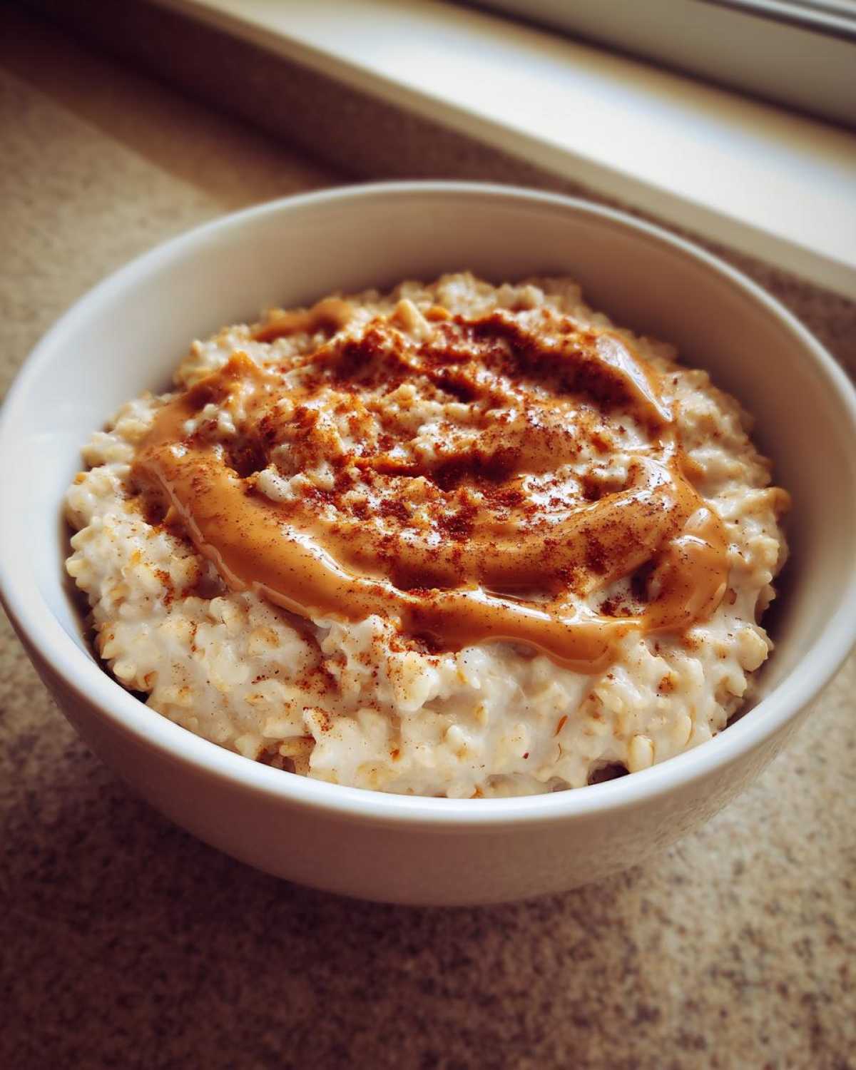 Close-up of creamy banana oatmeal topped with a swirl of melted peanut butter and a dusting of cinnamon.
