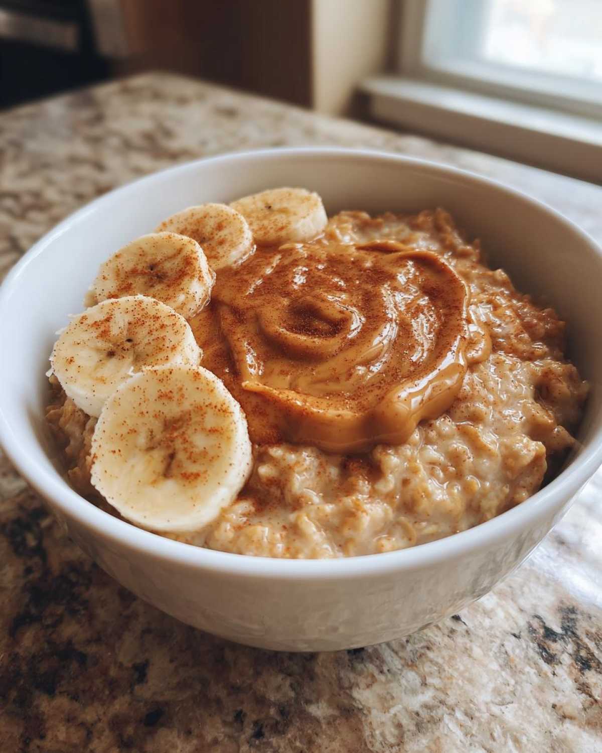 A close-up of creamy banana oatmeal topped with a swirl of peanut butter and sliced bananas dusted with cinnamon.