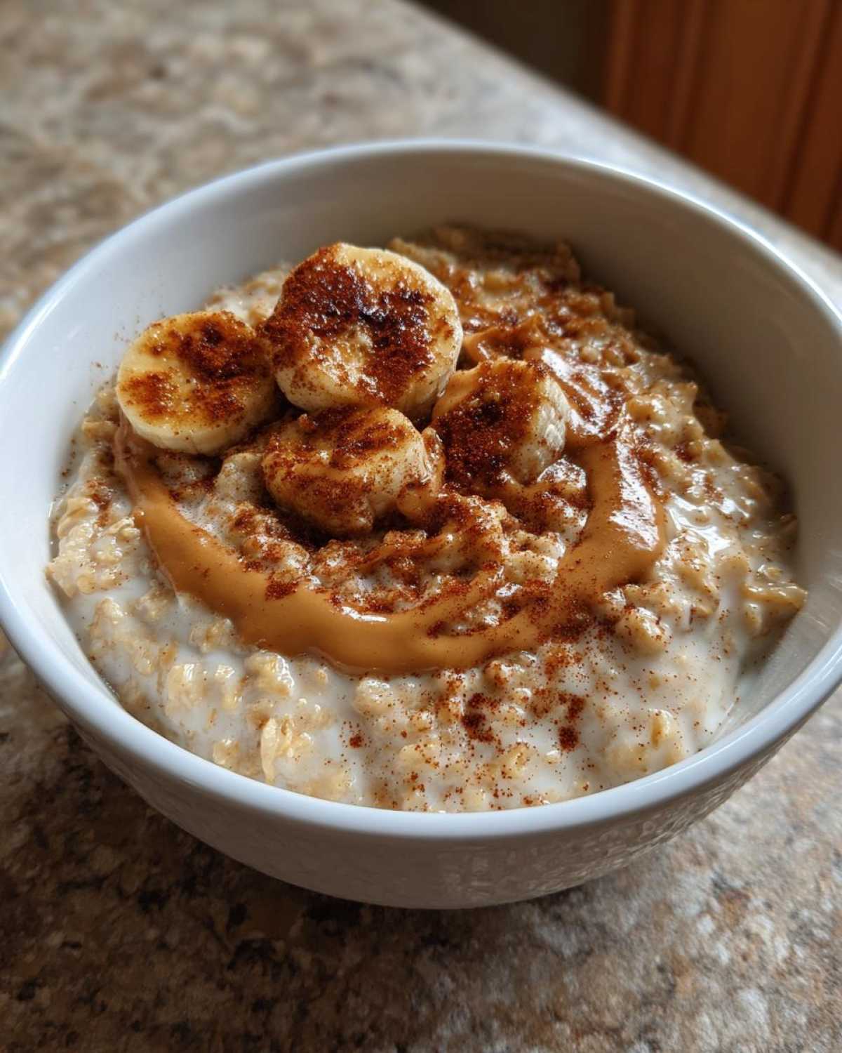 Close-up of creamy banana oatmeal topped with sliced bananas, peanut butter drizzle, and cinnamon.