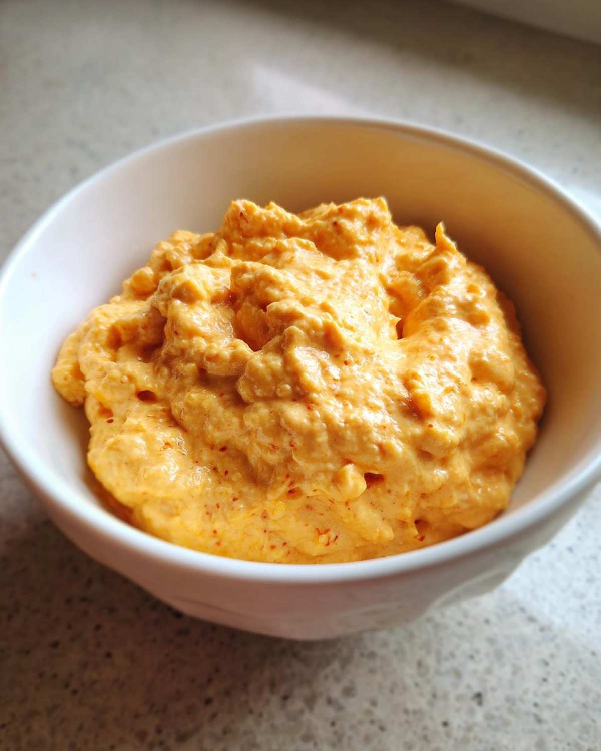 A close-up shot of thick, creamy, orange-colored beer cheese dip served in a small white bowl.