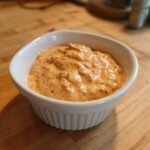 A close-up of creamy, orange-tinted big mac sauce with visible relish pieces in a small white ramekin.