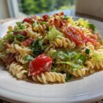 A close-up serving of creamy blt pasta salad featuring fusilli pasta, crisp lettuce, bacon bits, and halved cherry tomatoes on a white plate.