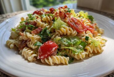 A close-up serving of creamy blt pasta salad featuring fusilli pasta, crisp lettuce, bacon bits, and halved cherry tomatoes on a white plate.