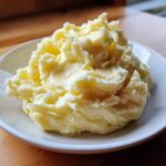 A close-up of fluffy, rich Boursin mashed potatoes piled high on a white plate.