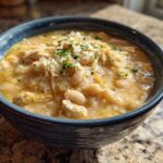 A close-up of a hearty bowl of creamy chicken chili topped with shredded chicken and chives.