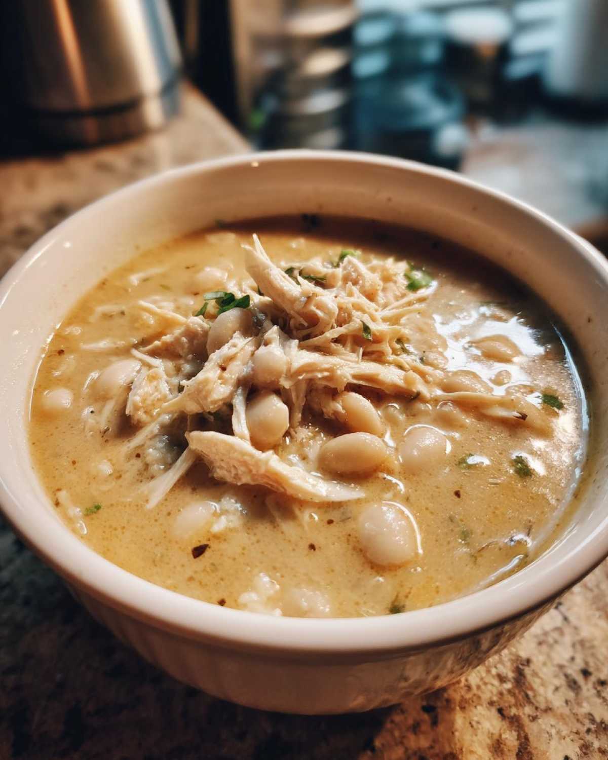 Close-up of a creamy white chicken chili bowl topped with shredded chicken and white beans.