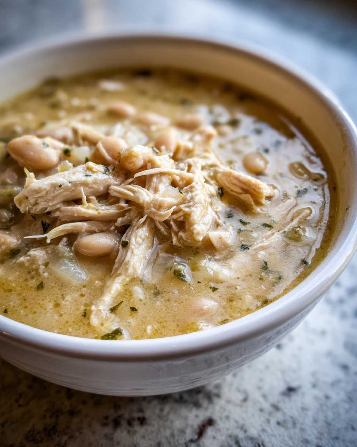 Close-up of a creamy white chicken chili topped with shredded chicken and white beans.