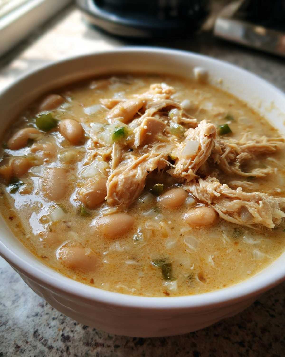 A close-up of a bowl of creamy chicken chili featuring shredded chicken, white beans, and green peppers.