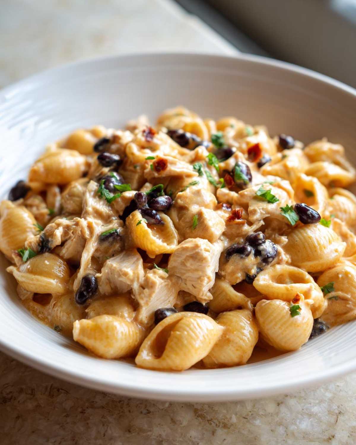 Close-up of creamy chicken enchilada pasta made with shell pasta, chicken chunks, black beans, and garnished with parsley.