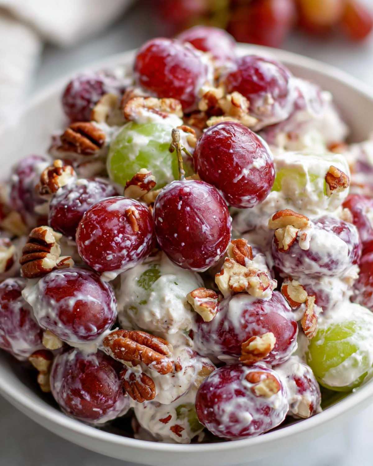 A close-up of creamy chicken salad chick grape salad featuring red and green grapes coated in a white dressing and topped with pecans.