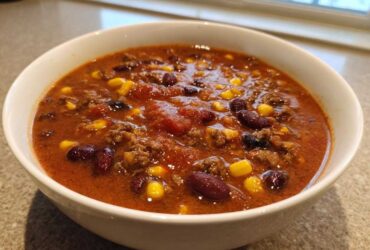 Close-up of a white bowl filled with rich, red cowboy soup containing ground beef, kidney beans, and corn kernels.