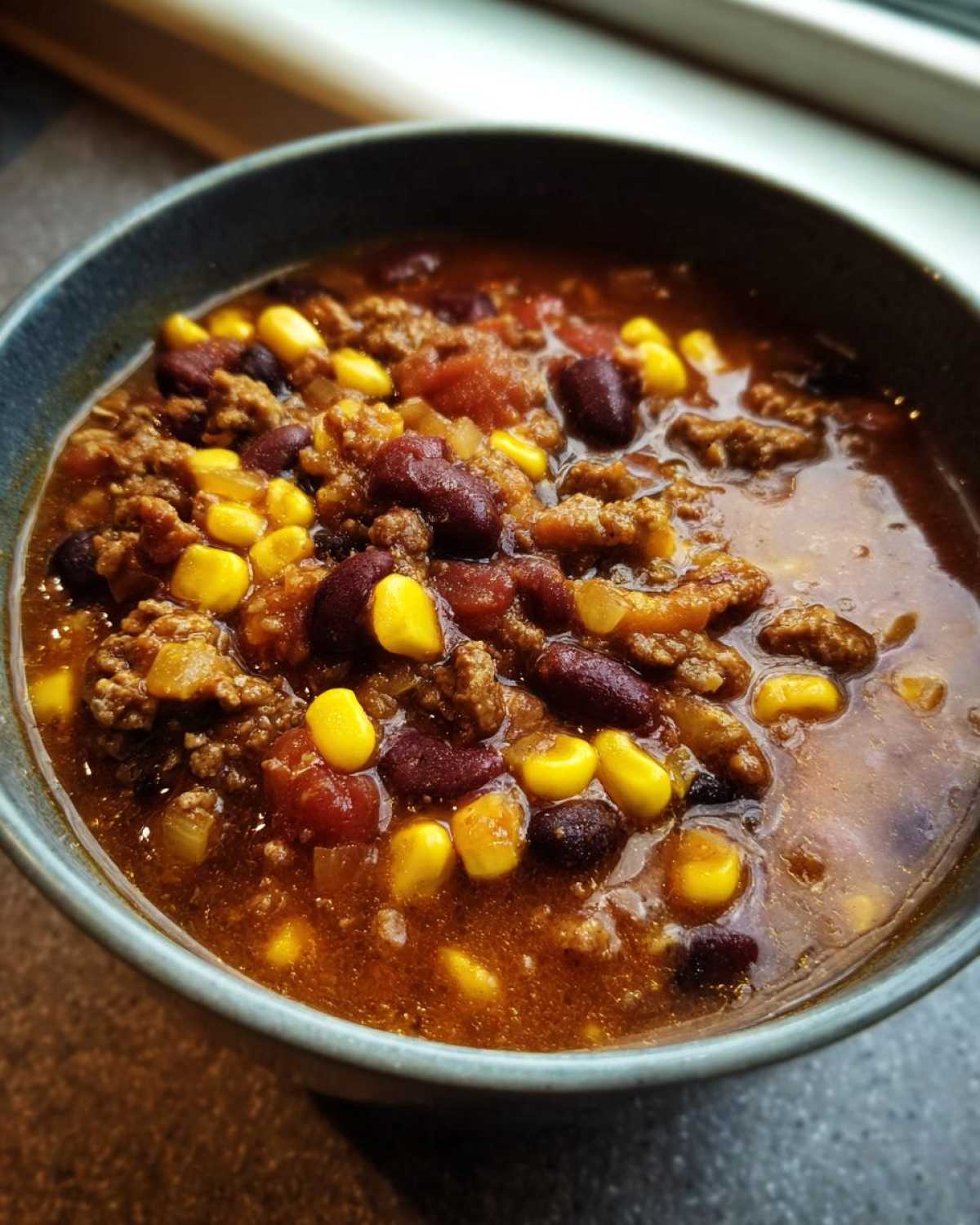 Close-up of a bowl filled with creamy cowboy soup featuring ground beef, kidney beans, and bright yellow corn kernels.