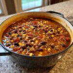 Close-up of rich, creamy cowboy soup filled with ground beef, corn, tomatoes, and beans in a cast iron pot.