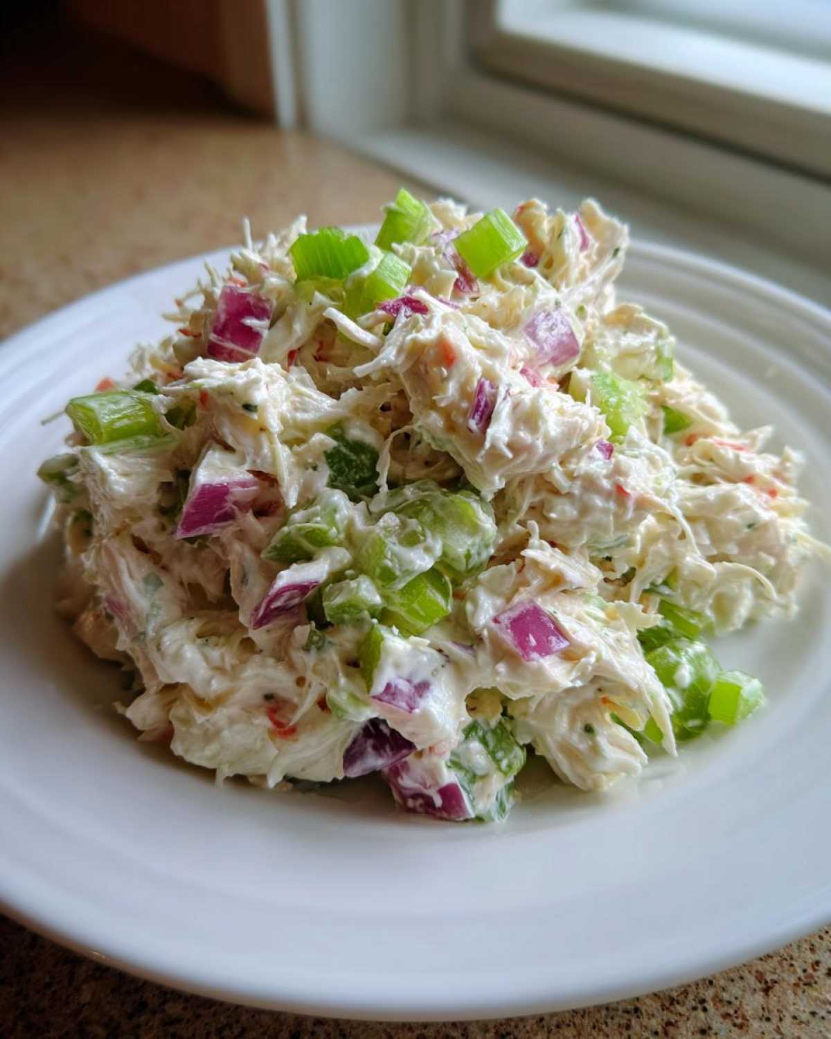 A mound of creamy crab salad mixed with chopped celery and red onion on a white plate.