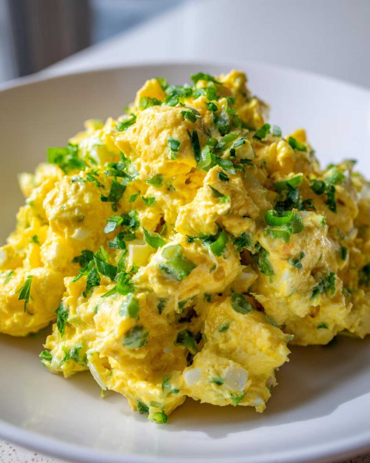 A close-up of creamy, bright yellow egg salad recipe generously topped with freshly chopped green chives.