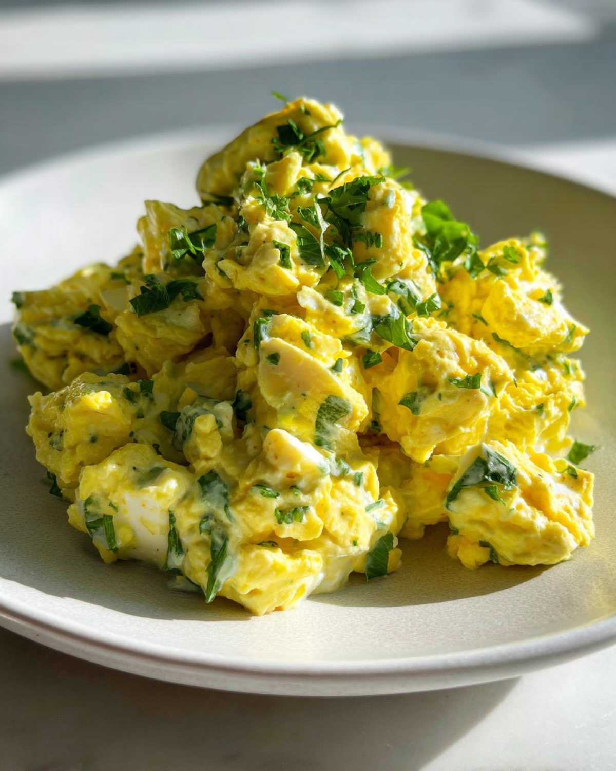 A mound of bright yellow egg salad recipe, mixed with creamy dressing and topped with fresh chopped parsley.