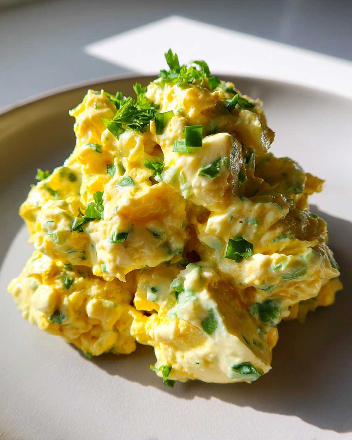 Close-up of a mound of creamy, yellow egg salad recipe garnished with fresh chopped green herbs.