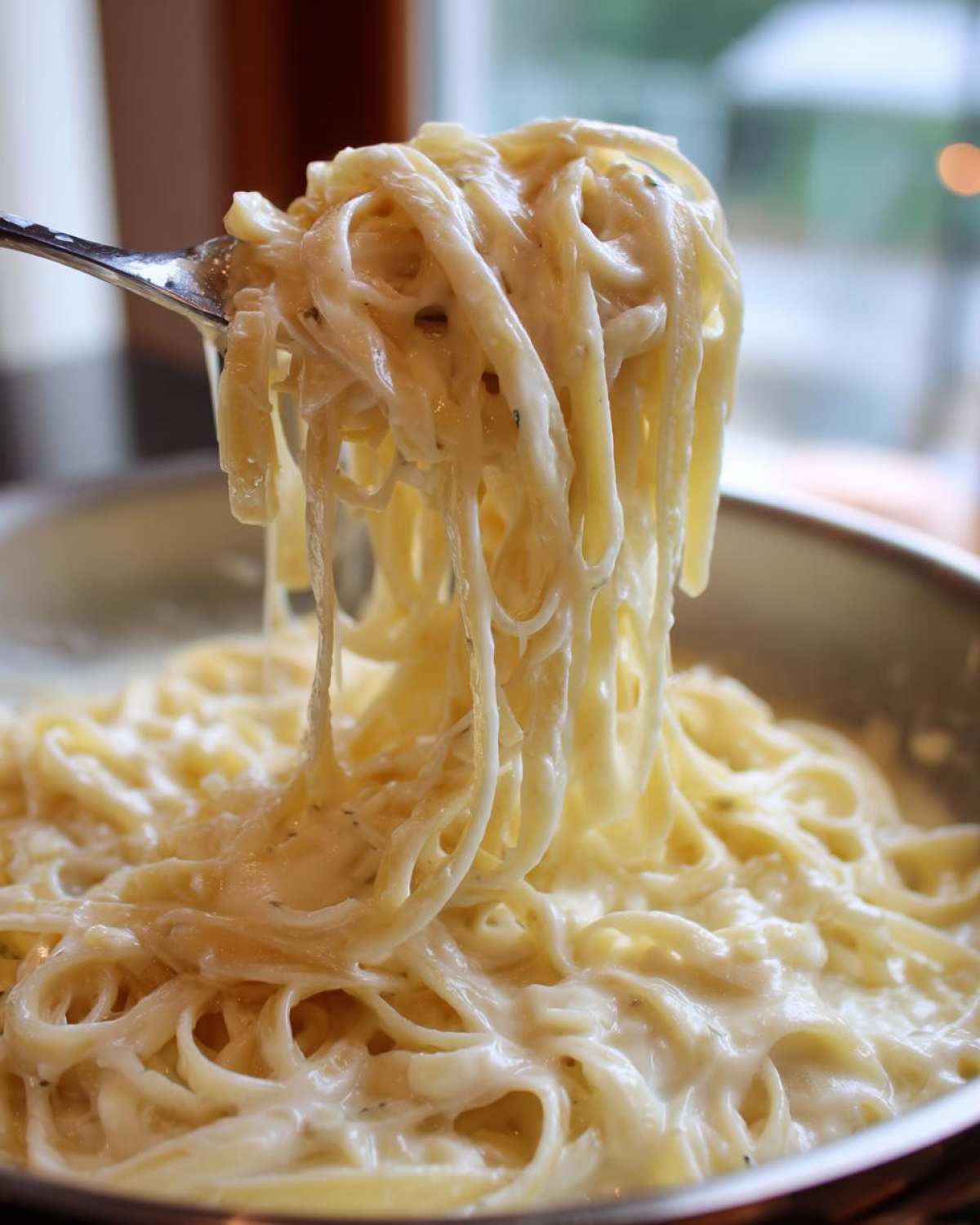 Close-up of fettuccine pasta coated in rich, creamy homemade alfredo sauce being lifted by a fork.