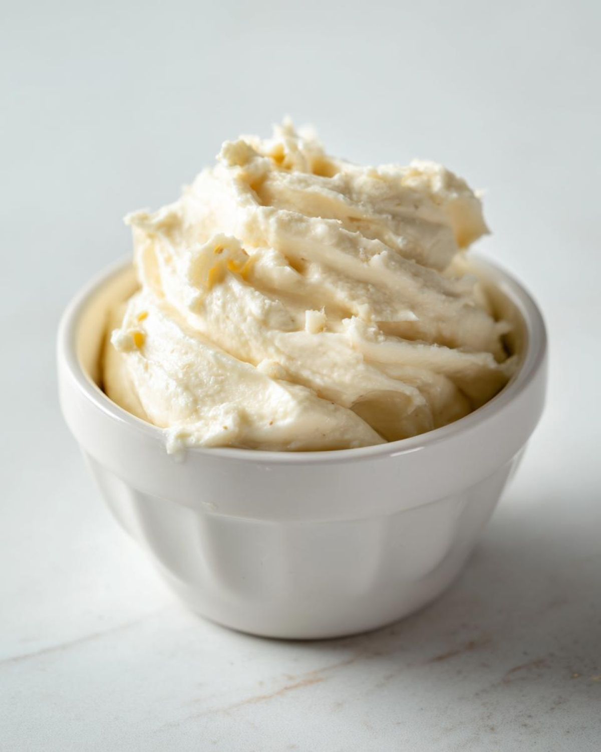 Close-up of thick, creamy homemade garlic aioli swirled high in a small white ramekin.
