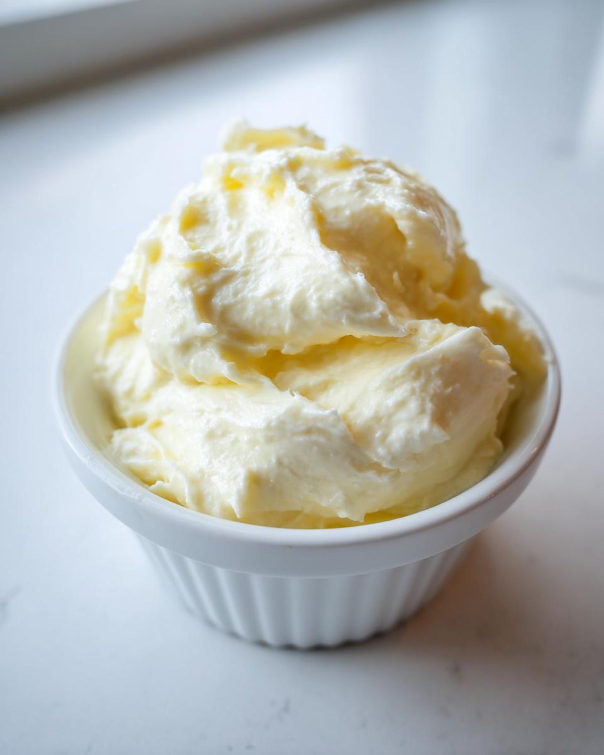 Close-up of creamy, pale yellow homemade garlic aioli piled high in a small white ramekin.