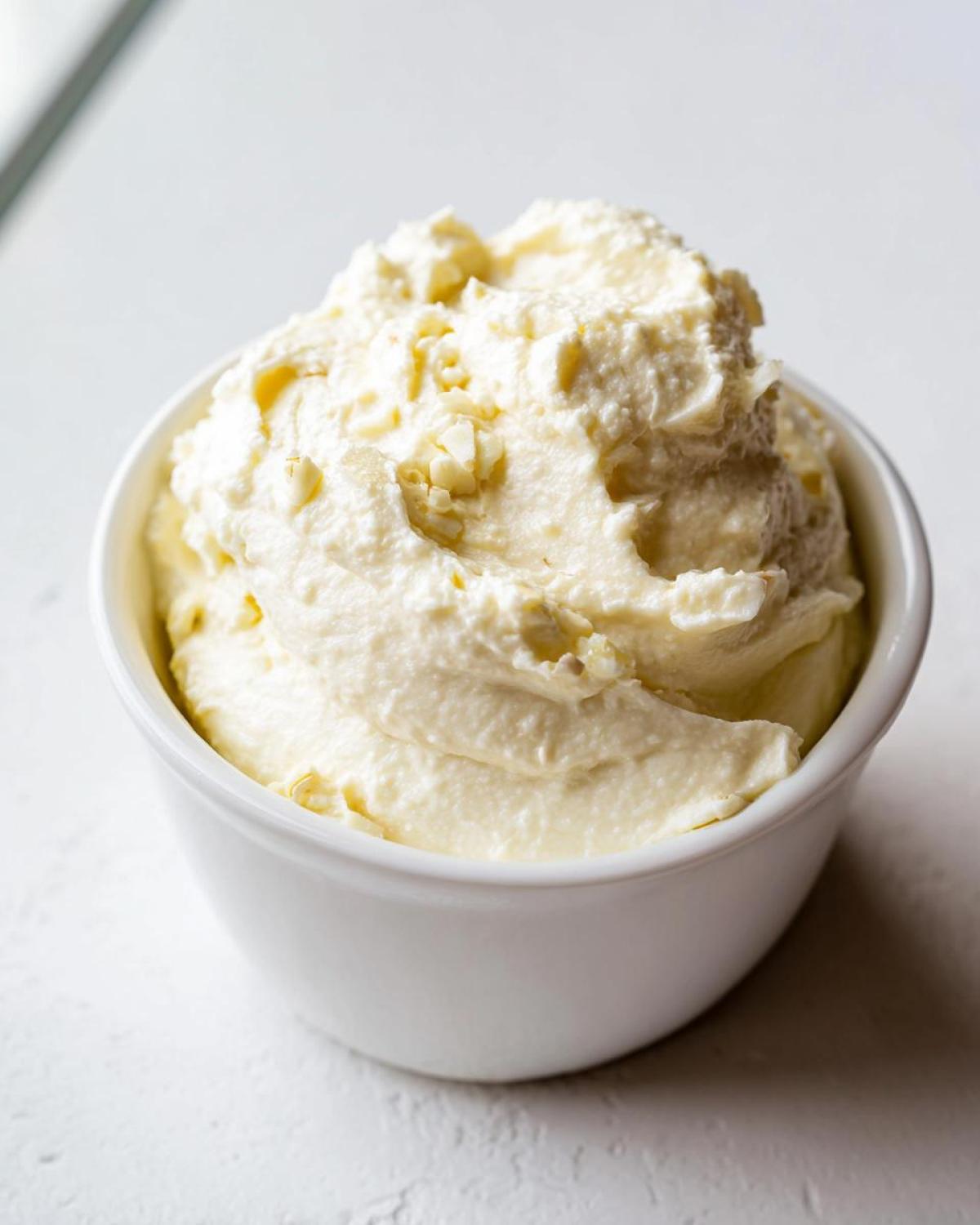 Close-up of a small white bowl filled with thick, creamy garlic aioli, showing texture and small chunks of garlic.
