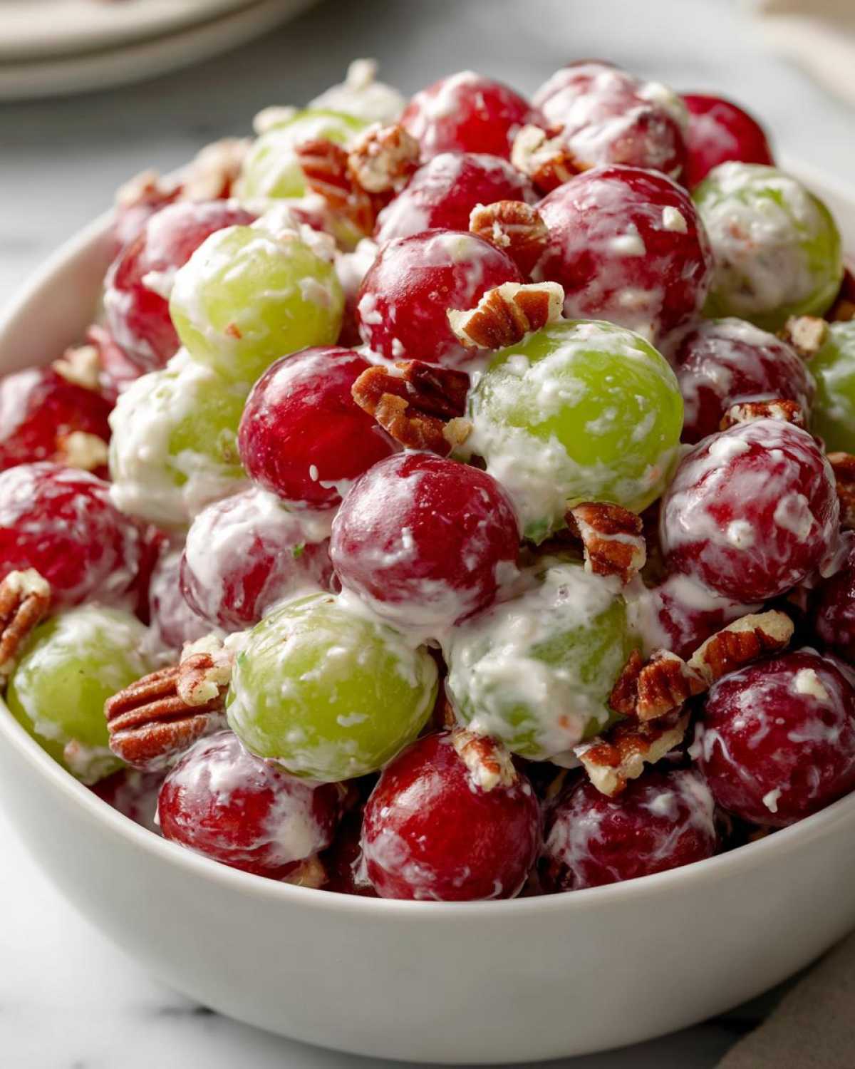 Close-up of creamy chicken salad chick grape salad featuring red and green grapes coated in a sweet dressing and topped with chopped pecans.