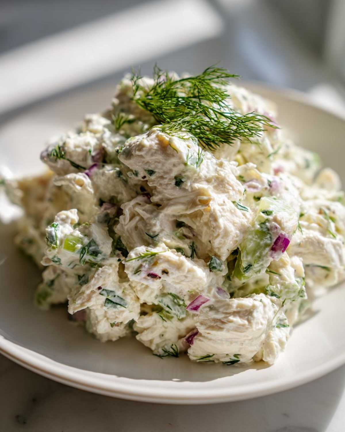 Close-up of a creamy serving of greek yogurt chicken salad mixed with red onion and celery, topped with fresh dill.