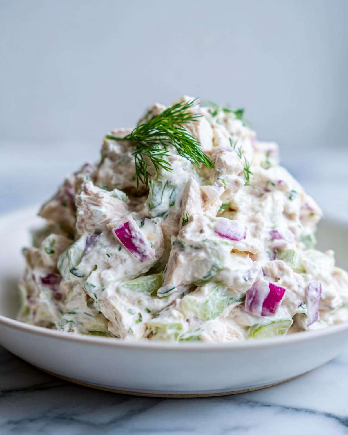 A mound of creamy greek yogurt chicken salad mixed with celery and red onion, garnished with fresh dill.