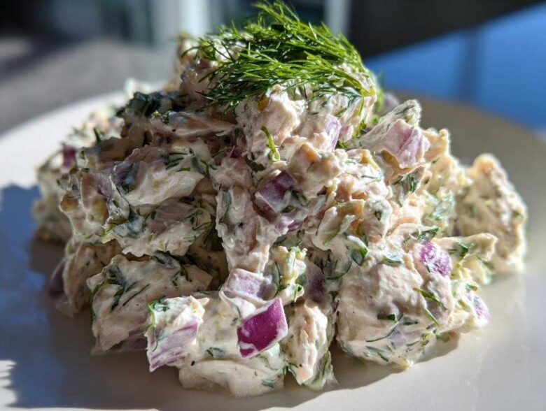 A close-up, bright photo of creamy greek yogurt chicken salad mixed with chunks of red onion and topped with fresh dill.