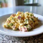 A scoop of creamy ham salad recipe mixed with diced ham and green peppers served on a white plate.