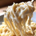 Close-up of pasta twirled on a fork, heavily coated in rich, creamy homemade alfredo sauce.