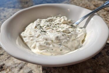 Close-up of a white bowl filled with thick, creamy horseradish sauce, garnished with dried herbs.
