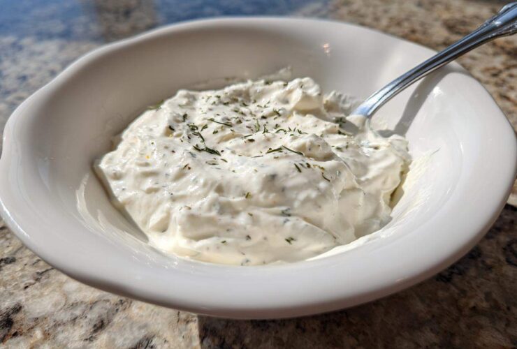 Close-up of a white bowl filled with thick, creamy horseradish sauce, garnished with dried herbs.