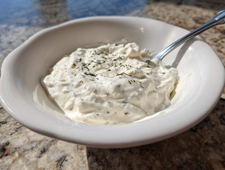 Close-up of a white bowl filled with thick, creamy horseradish sauce, garnished with dried herbs.