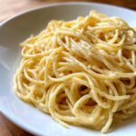 A close-up shot of perfectly twirled spaghetti coated in a rich, creamy lemon pasta sauce, seasoned with black pepper.