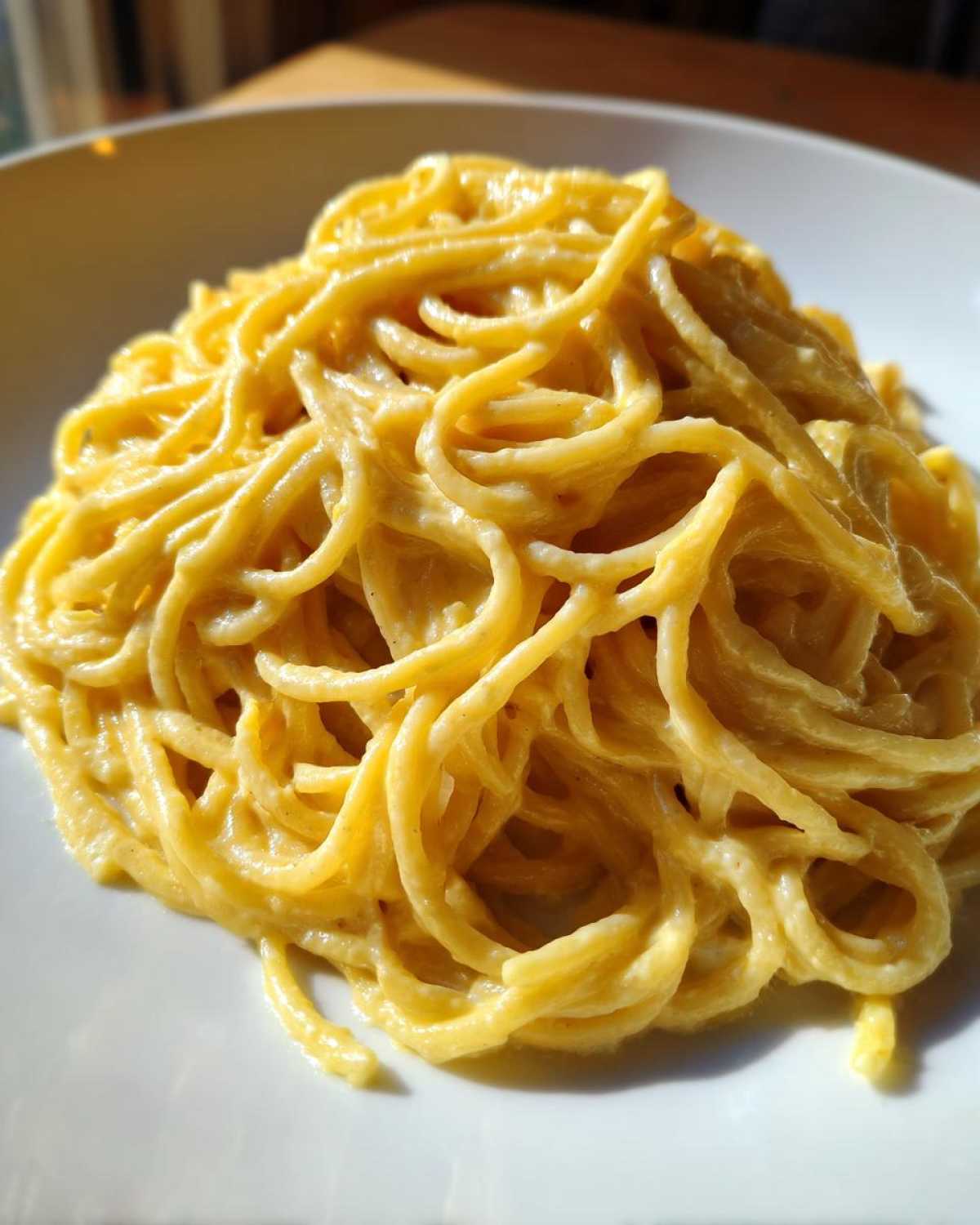 A close-up, vibrant shot of spaghetti coated in rich, creamy lemon pasta sauce served on a white plate.