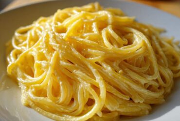 A close-up shot of spaghetti coated in a rich, bright sauce for creamy lemon pasta served on a white plate.