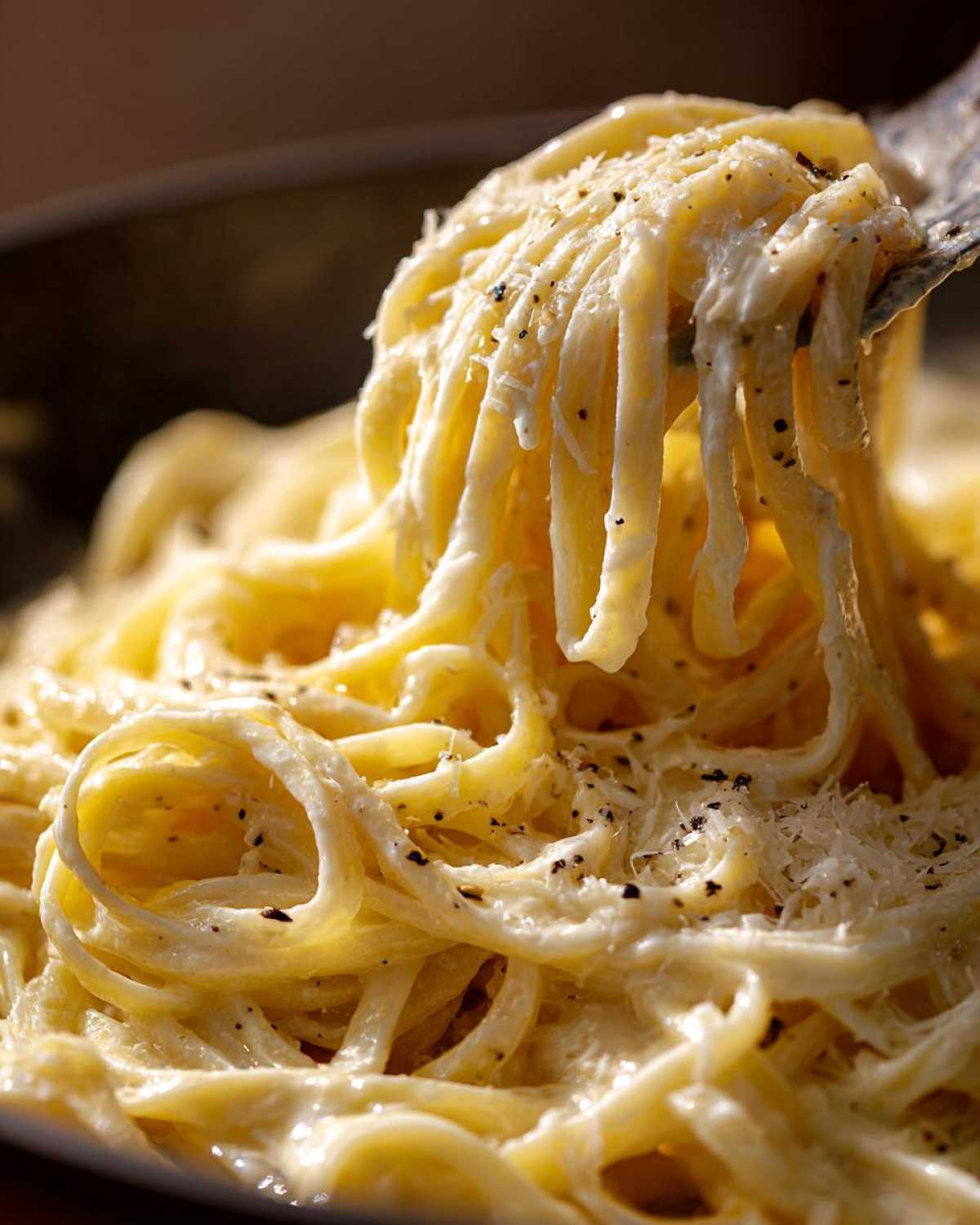 Close-up of fettuccine noodles coated in rich, creamy Olive Garden Alfredo Sauce, topped with black pepper.