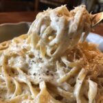 Close-up of fettuccine pasta coated heavily in creamy Olive Garden Alfredo Sauce, lifted by a fork.