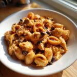Close-up of creamy enchilada pasta with chicken chunks and black beans served in a white bowl.
