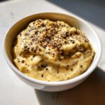 A close-up of thick, creamy peppercorn sauce generously topped with cracked black peppercorns in a white bowl.