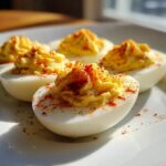 Close-up of creamy, piped deviled eggs dusted generously with paprika on a white plate.