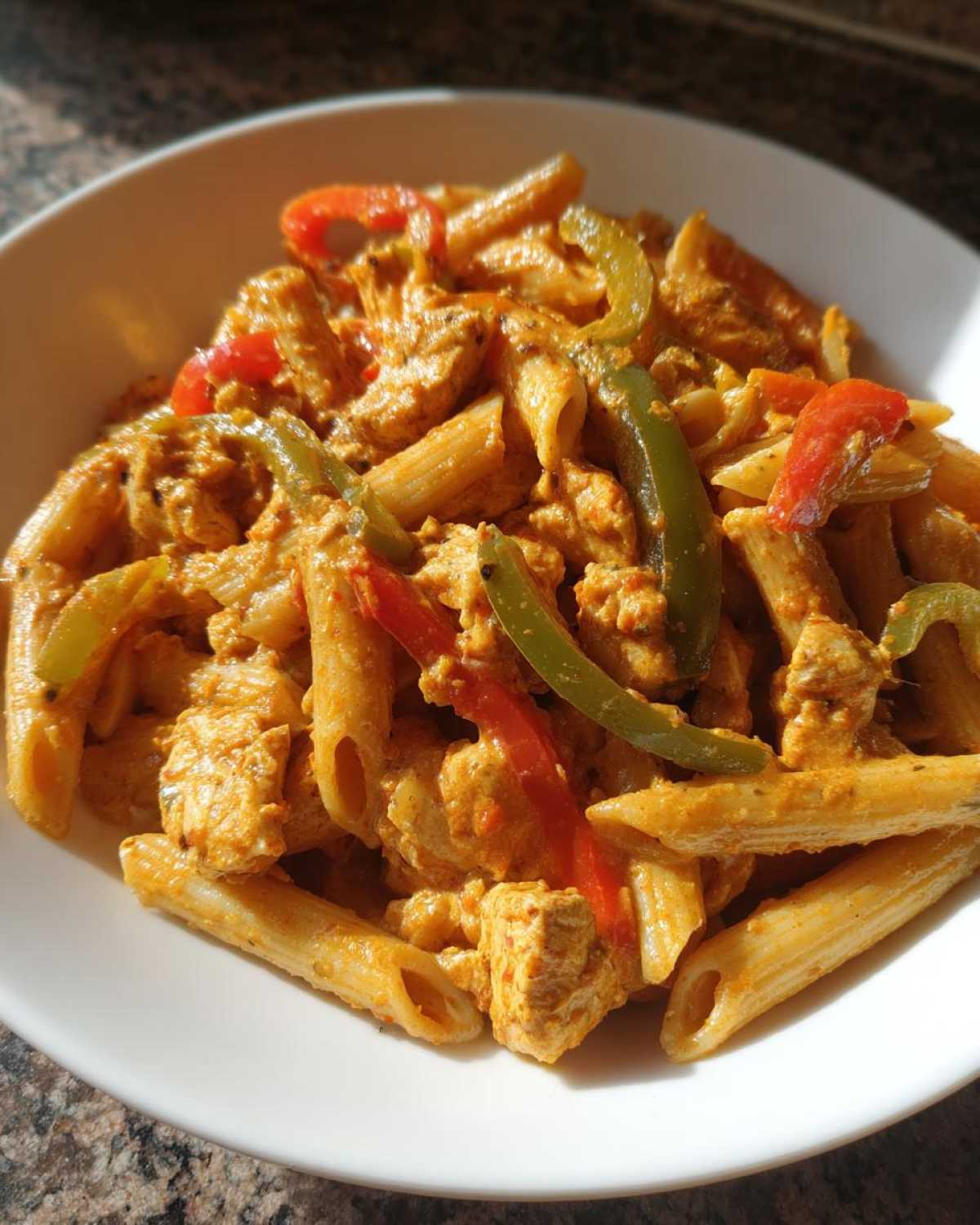 A close-up shot of creamy Rasta Pasta featuring penne, chicken pieces, and sliced red and green bell peppers.