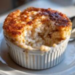 Close-up of creamy baked rice pudding in a white ramekin, topped with browned sugar and cinnamon.
