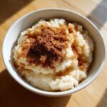 A close-up of creamy rice pudding recipe served in a white bowl, generously dusted with ground cinnamon.