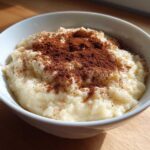 A close-up of a white bowl filled with creamy rice pudding recipe, generously dusted with cinnamon.